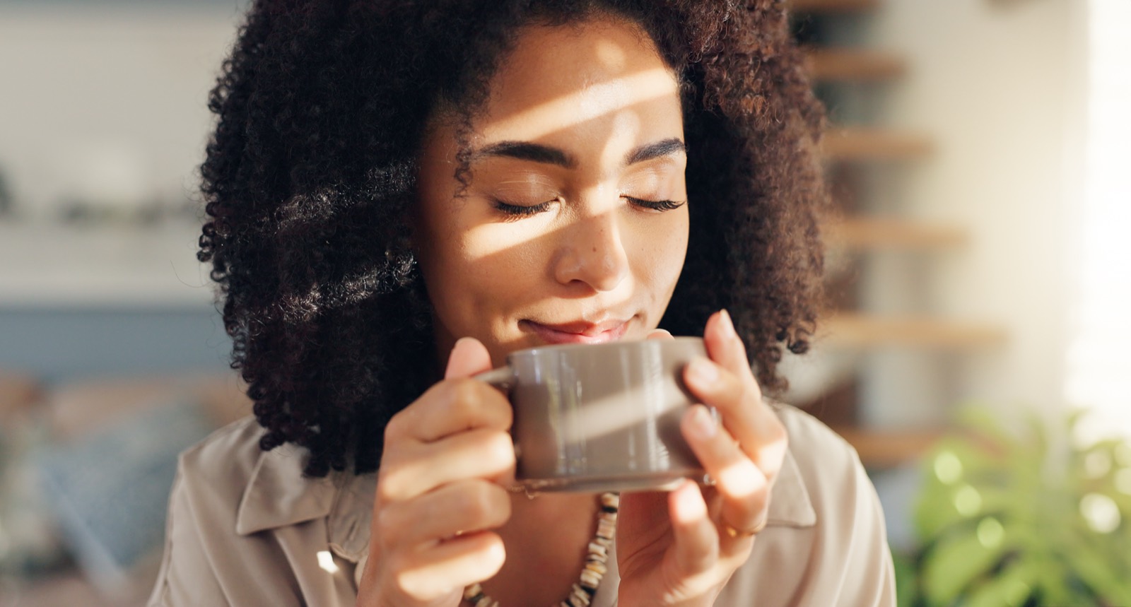 A woman sitting calmly by a window with a warm drink