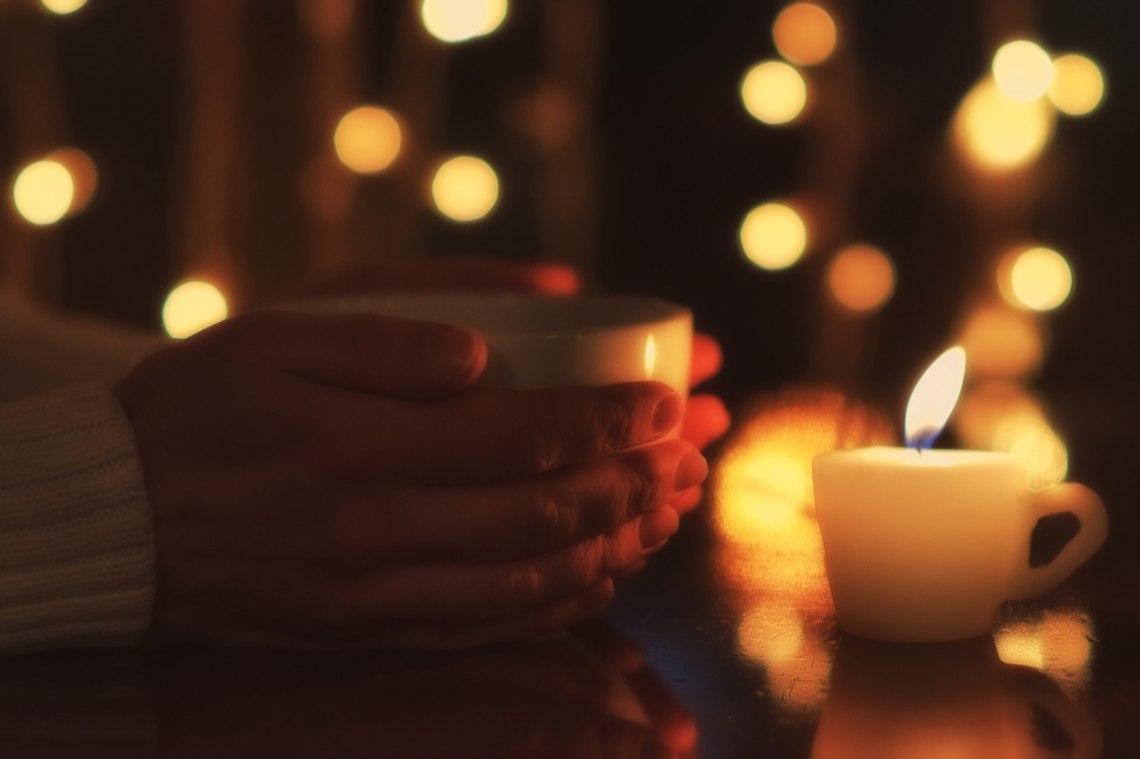 Hands holding a cup of tea beside a softly burning candle